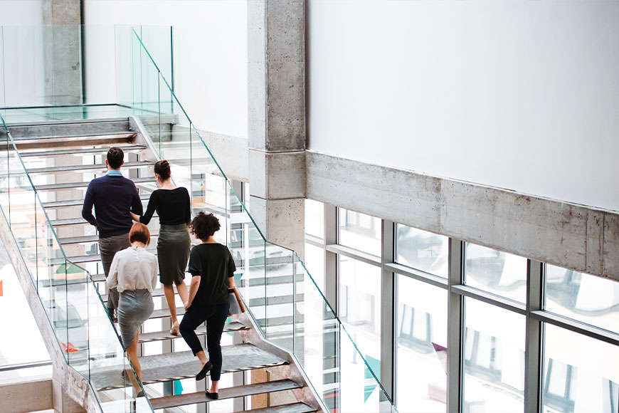 Four colleagues walking down a glass staircase in a modern office atrium